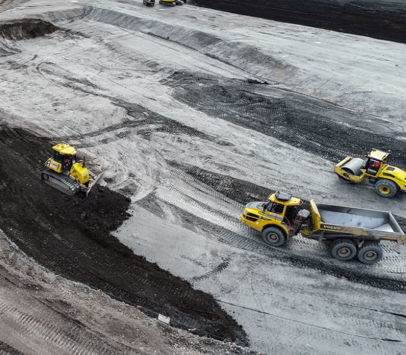 Removal of existing concrete and hardstandings from the site featuring yellow diggers, rollers & material transportation vehicles.