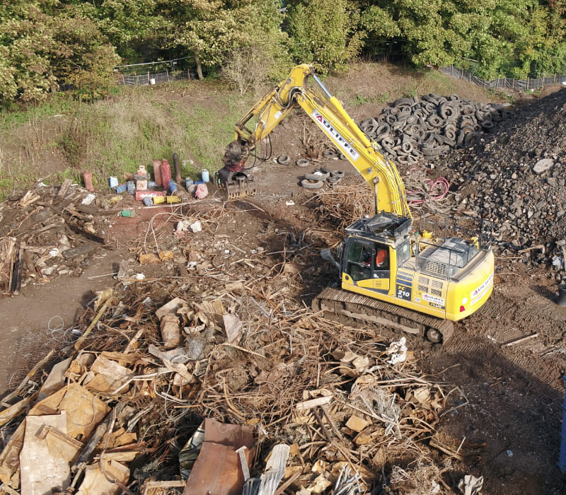 Yellow McAuliffe branded digger surrounded by waste that was collected during the remediation process.